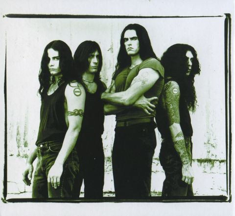 1967 Ford Custom Wagon - Four men with long dark hair and tattoos stand in front of a textured white wall. The image has a green tint.