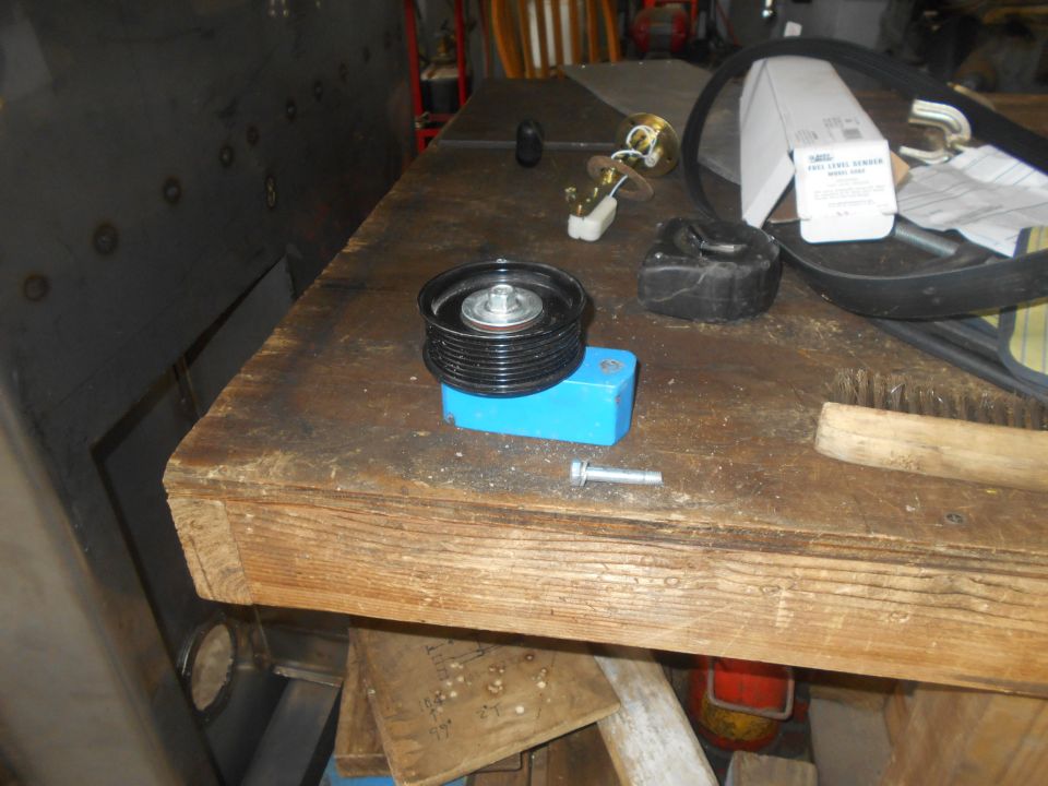 Automotive parts including a serpentine belt, fuel sender, pulley, and bolt on a workbench.