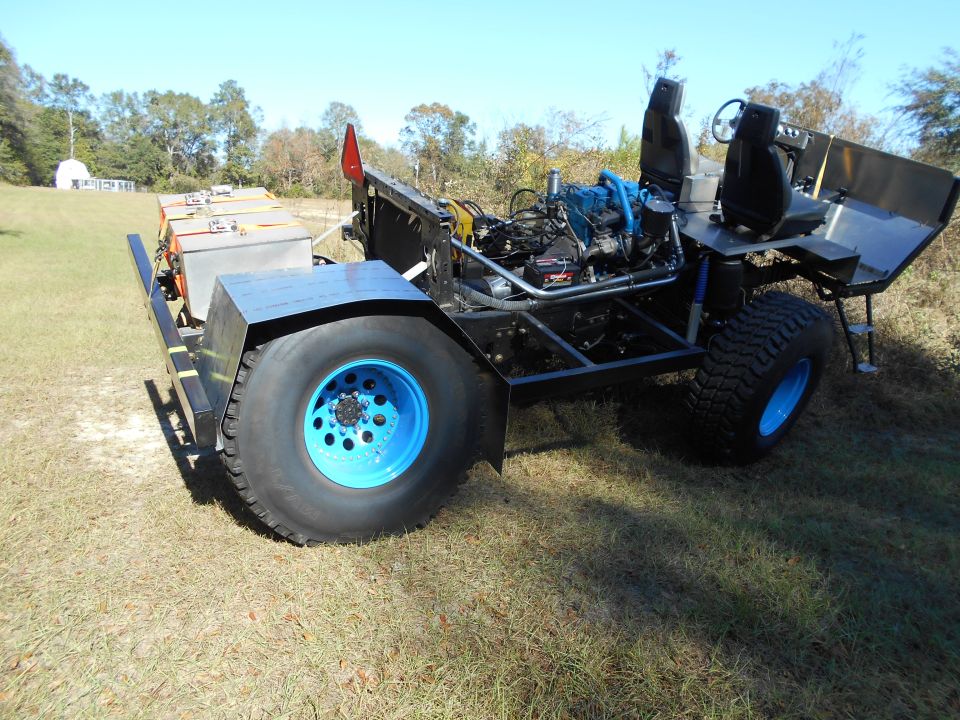Custom off-road vehicle with blue engine, seats, and rims, towing battery boxes.