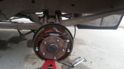 1985 Ford Bronco - A close-up view of the rear drum brake assembly of a vehicle, supported by a red jack stand. The brake drum is removed, revealing the shoes…