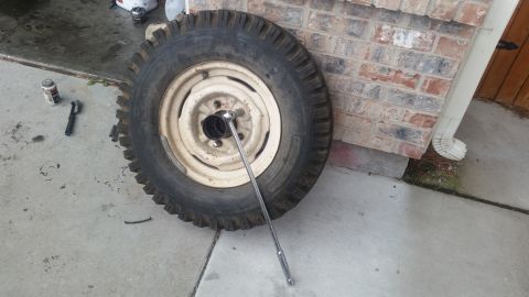 1985 Ford Bronco - A tire and rim assembly is shown on a concrete surface next to a brick wall. A socket wrench is attached to one of the lug nuts.