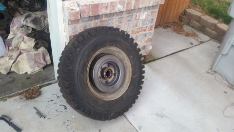 1985 Ford Bronco - A large tire with a brake rotor and hub assembly is shown resting on a concrete surface next to a brick wall. Tools and debris are scattere…
