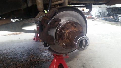 1985 Ford Bronco - Close-up of a vehicle's brake assembly, including a Warn locking hub, supported by a red jack stand.