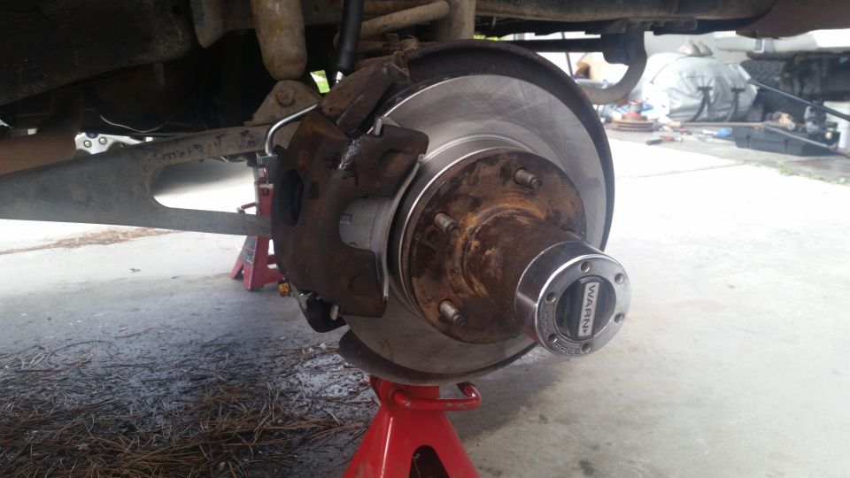 Vehicle brake assembly on red jack stand, showing rotor, caliper, and Warn hub