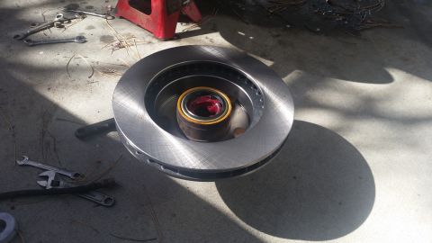 1985 Ford Bronco - A new brake rotor and bearing assembly sits on a concrete surface with tools nearby.