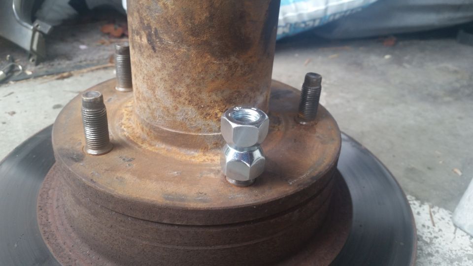 Wheel hub with two lug nuts stacked on top of each other, showing rusty metal and brake rotor