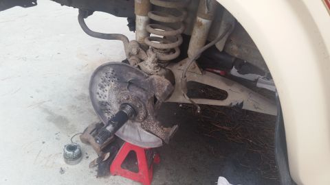 1985 Ford Bronco - Close-up view of a vehicle's front wheel assembly, including brake components and suspension, supported by a red jack stand.