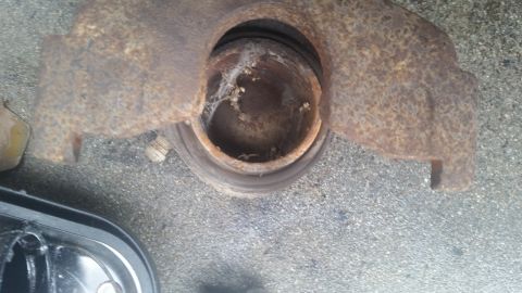 1985 Ford Bronco - This heavily rusted brake caliper and rotor assembly is shown from a top-down perspective on a paved surface.
