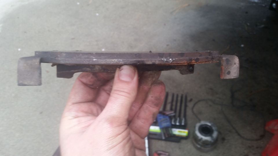 Worn brake pad held in hand, with tools in background