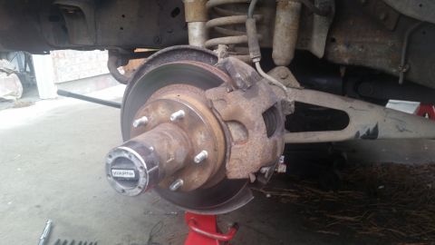 1985 Ford Bronco - Close-up view of a vehicle's front brake assembly, showing rust and wear on the rotor and caliper.
