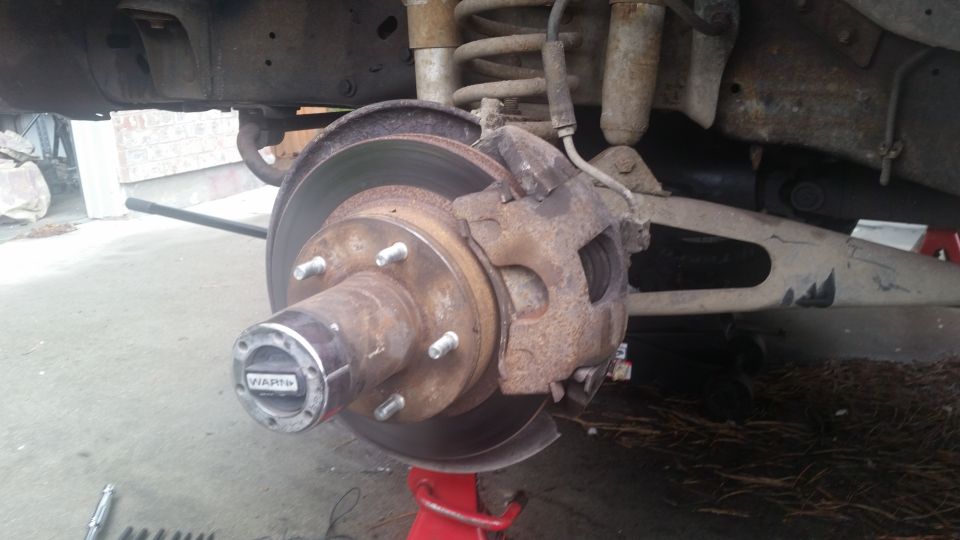 close-up of rusty vehicle brake rotor, caliper, and hub with 'WARN' text on hub
