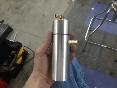 1994 Ford Bronco - A person holds an aluminum oil catch can with two brass fittings, one on top and one on the side.
