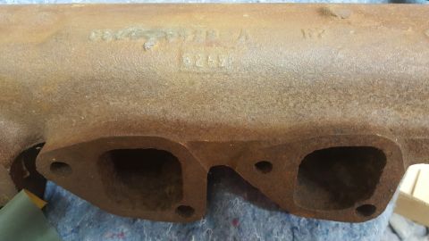 1973 Ford Mustang - This is a close-up view of a rusty exhaust manifold with visible stamped markings.