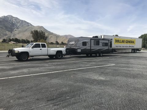 2018 Yugo GV - A white pickup truck tows a travel trailer and a Dollar General semi-trailer in a parking lot.