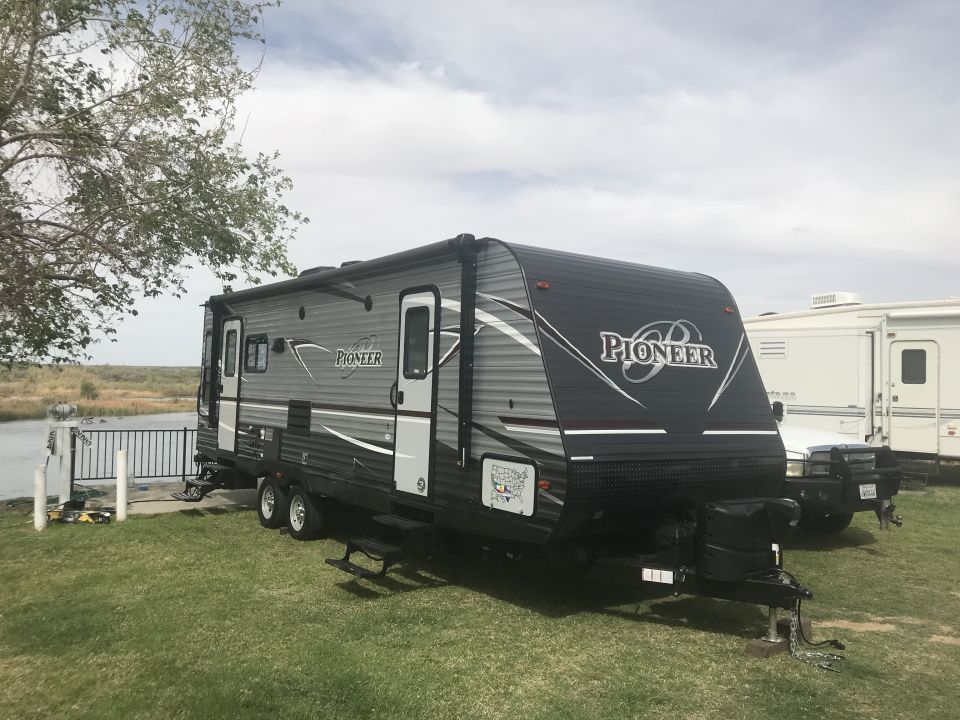 Travel trailer with 'Pioneer' branding parked by a lake
