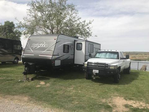 2018 Yugo GV - White pickup truck and Pioneer travel trailer parked on grass near a body of water.