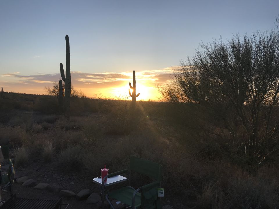 Desert sunset with saguaro cacti and scrub brush. A camping chair and small table are in the foreground