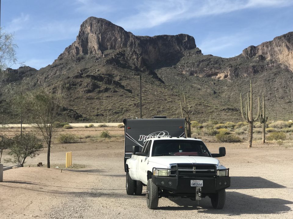 Dodge Ram 3500 towing a gray Pioneer trailer, parked in a desert with mountains and saguaro cacti