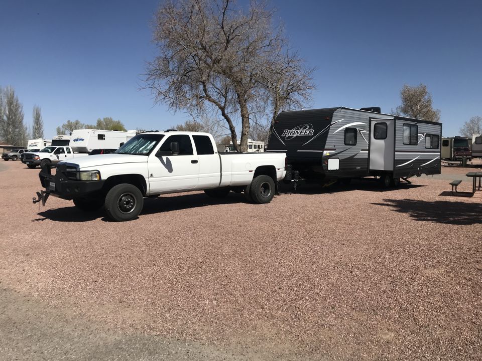White dually pickup truck towing a gray travel trailer with 'Pioneer' on the side