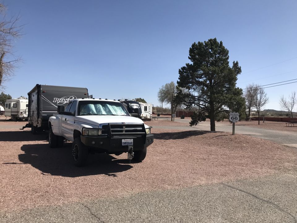 White pickup truck towing a travel trailer, parked at a campsite with a Route 66 sign
