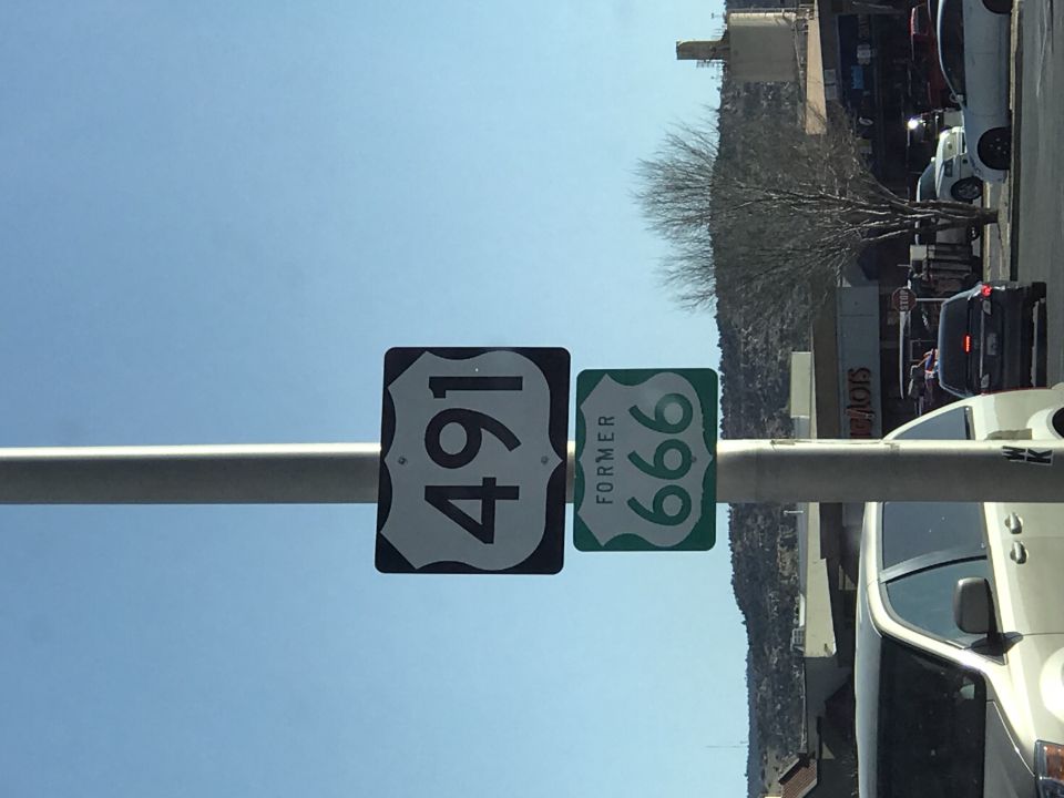 Route 491 and Former Route 666 signs on a pole, with cars and buildings in the background