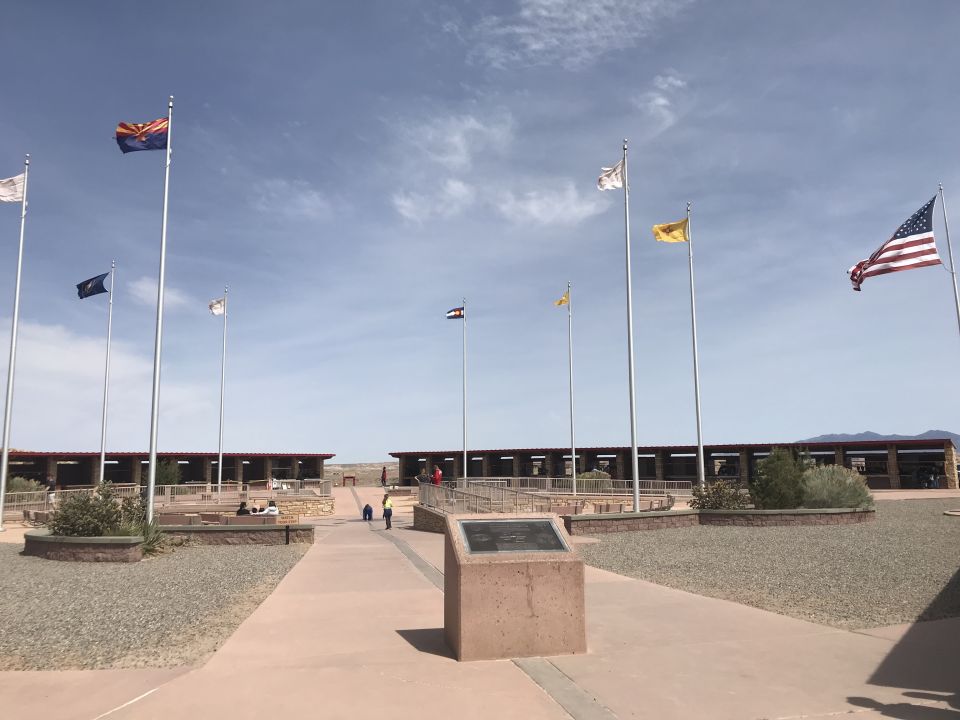 Flags fly in front of a long, covered building complex under a partly cloudy sky