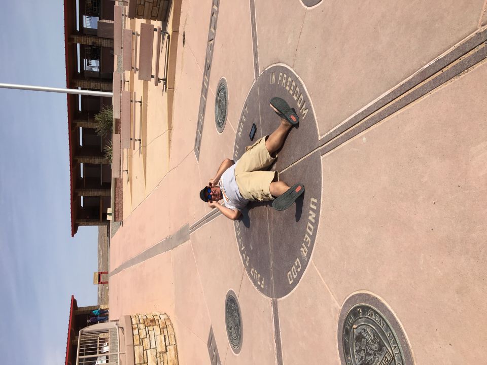 Guy lying on the ground at the Four Corners Monument, with his arms out