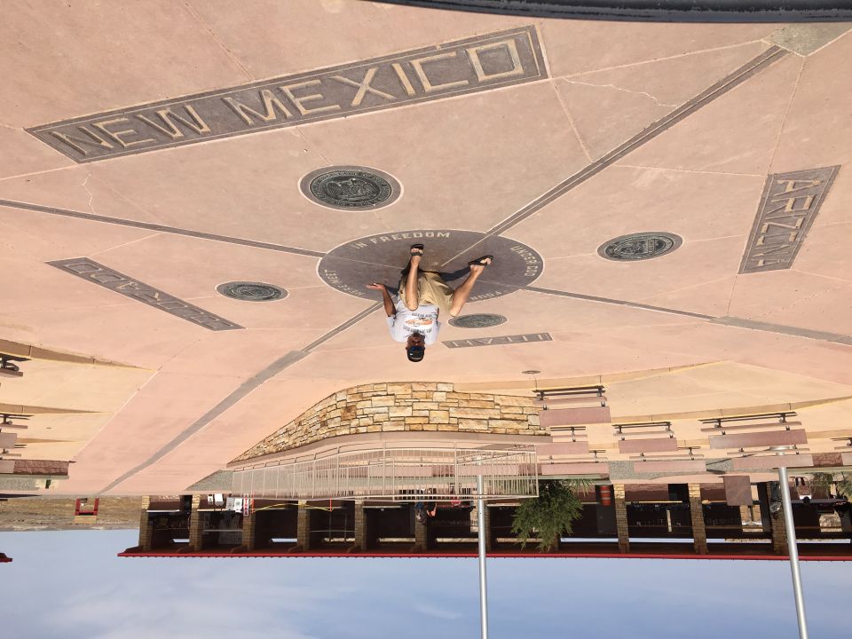 Person standing at the Four Corners Monument, with state names inscribed on the ground