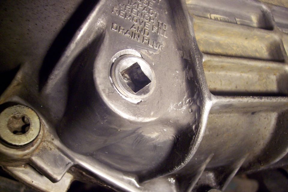 Close-up of a square-drive drain plug on a metal automotive housing with text.