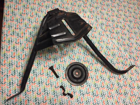 1967 Ford Custom Wagon - A black metal part, likely a bracket or support, is laid out on a patterned surface. It appears to be a component from a vehicle, possibly…