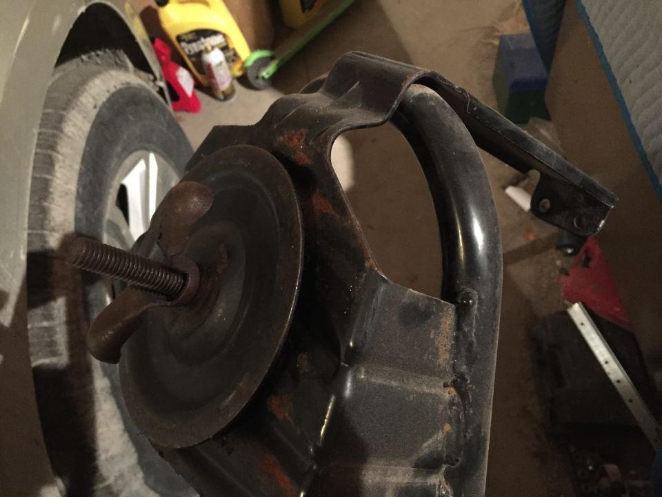 Rusty metal automotive part with threaded bolt and wingnut near a car tire.