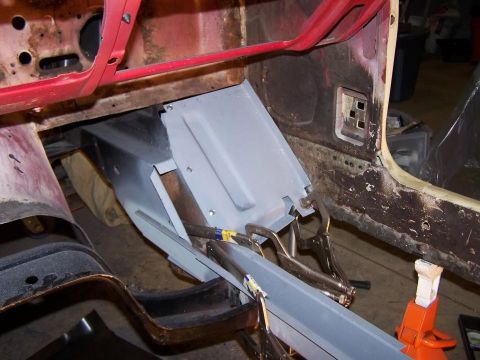 1965 Ford Mustang - A partially restored vehicle interior shows a gray metal panel being fitted into the floor area, secured with clamps and screws. The surrou…