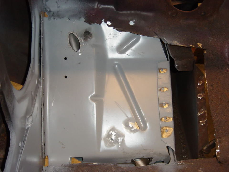 Close-up of a vehicle's gray painted floor pan with spot welds, possibly undergoing repair.