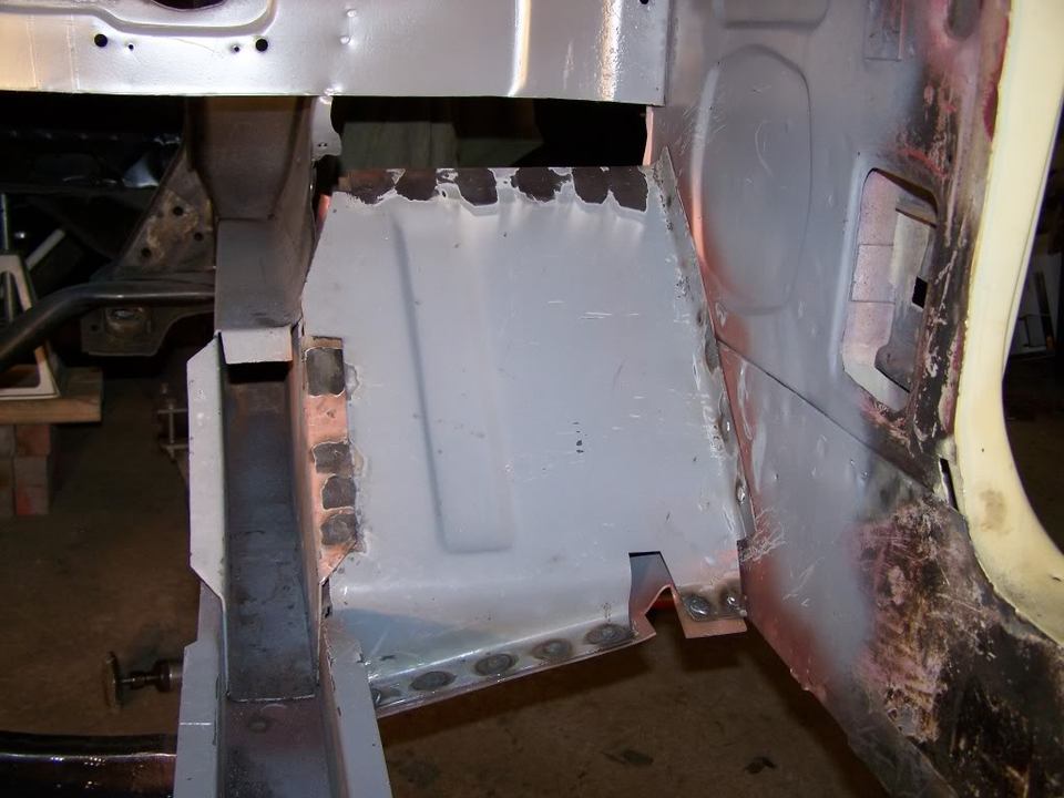 Driver's side floor pan and rocker panel area of a classic car undergoing restoration with new metal welded in place.