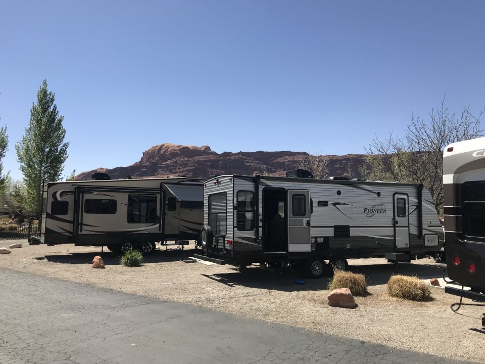 Two travel trailers parked on a gravel lot with mountains in the background.
