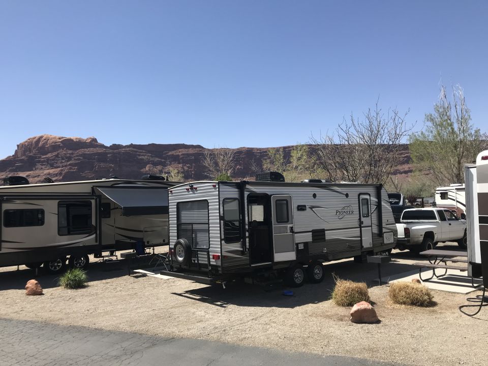 Silver and black Pioneer RL250 travel trailer parked at a campsite.