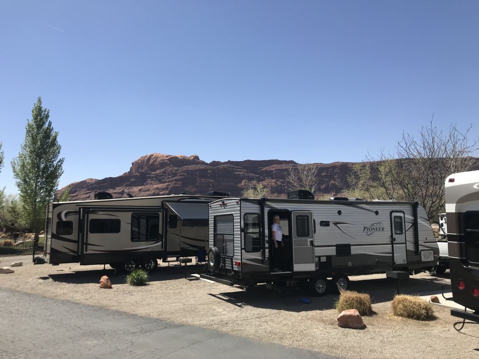 Two travel trailers parked in a desert campsite with mountains in the background.