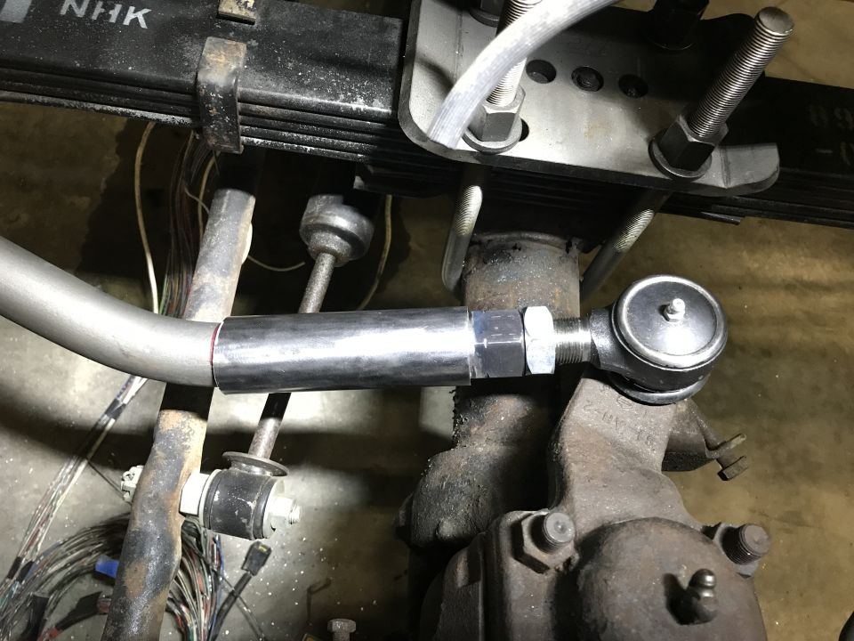 Modified tie rod end connected to steering knuckle, leaf spring assembly above. Vehicle part close-up.