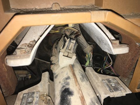 1980 Ford Bronco - A close-up view of the wiring harness and connectors under the dashboard of a 1980 Ford Bronco. The area is dusty and shows various wires a…
