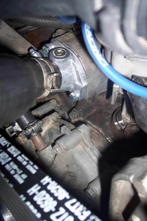 1995 Ford Bronco - A close-up view of a newly installed aluminum thermostat housing on a vehicle engine. The housing is secured with bolts and connected to a…