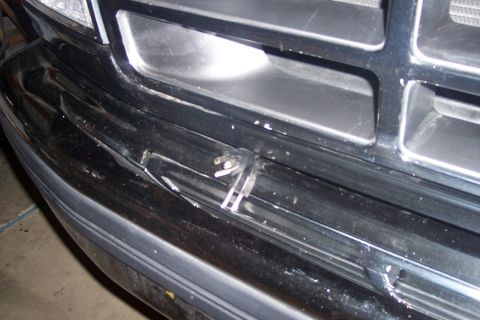 1995 Ford Bronco - A close-up view of a black vehicle's front bumper and grille shows damage and some detached plastic pieces. The grille has horizontal bars…