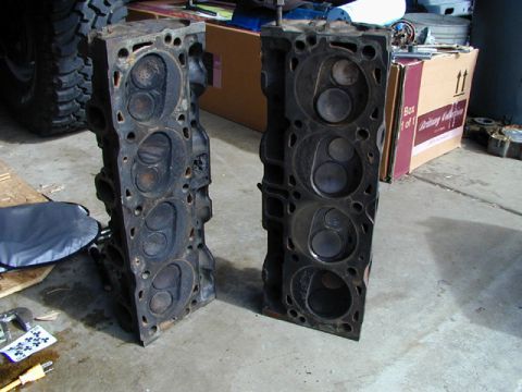 1979 Ford Bronco - Two used engine cylinder heads are displayed on a garage floor, with a tire and boxes in the background.