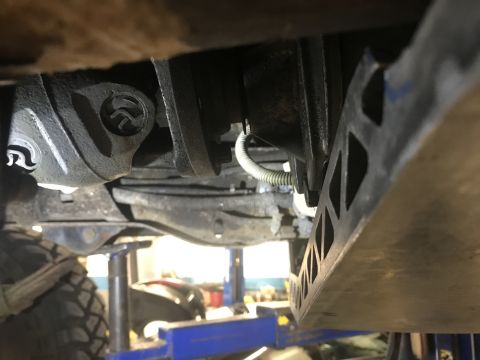 1995 Ford Bronco - Underside view of a vehicle's drivetrain, showing a driveshaft U-joint and a metal skid plate with a cut-out pattern. The vehicle appears t…