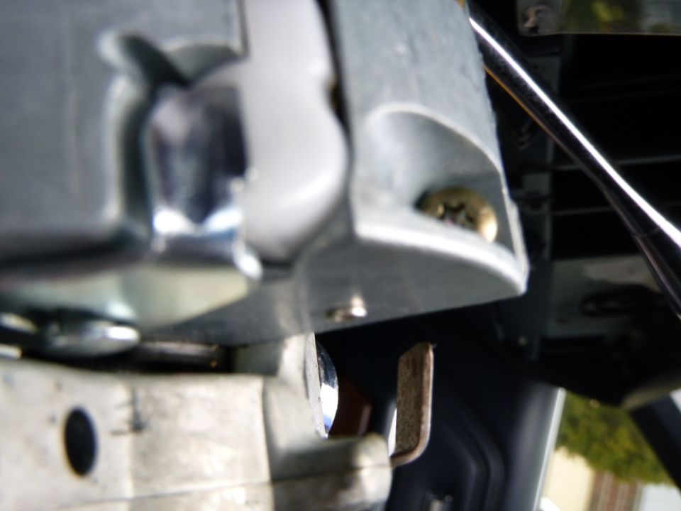 Close-up of vehicle interior steering column area with metal bracket and screw.