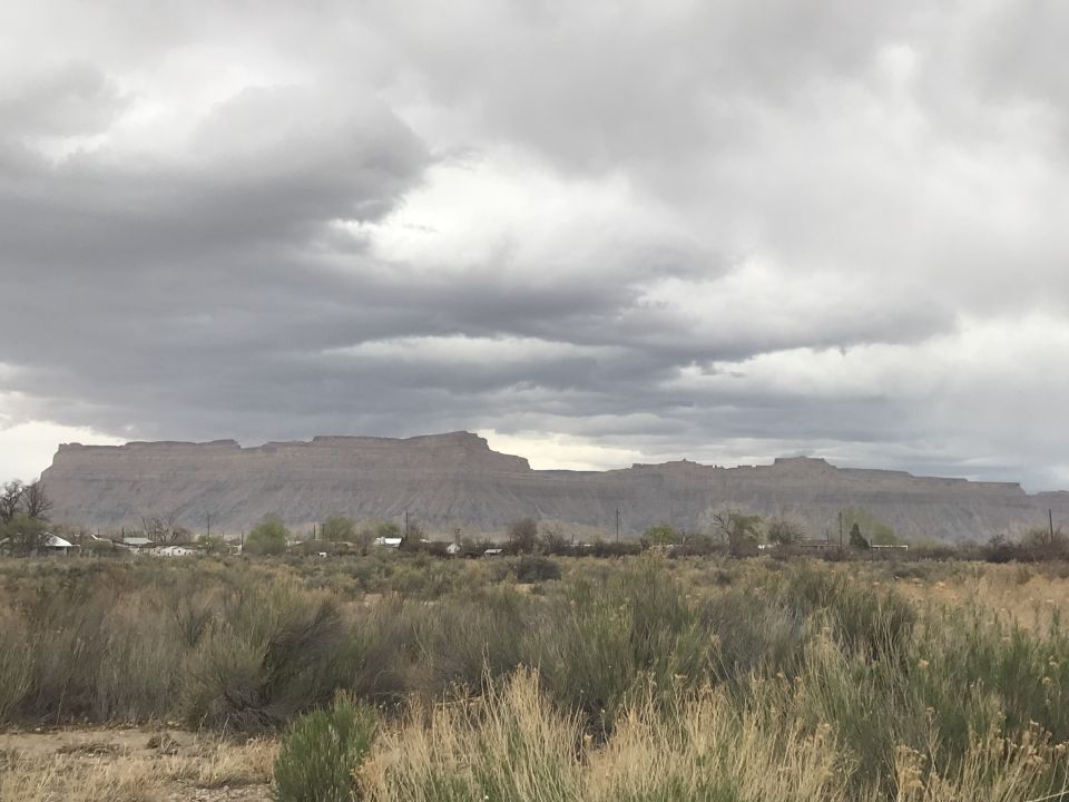 Mountain range with cloudy sky and foreground vegetation and buildings.