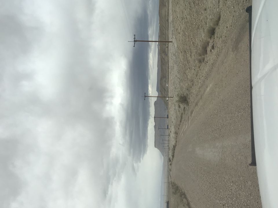 Dirt road with utility poles and mountains under a cloudy sky