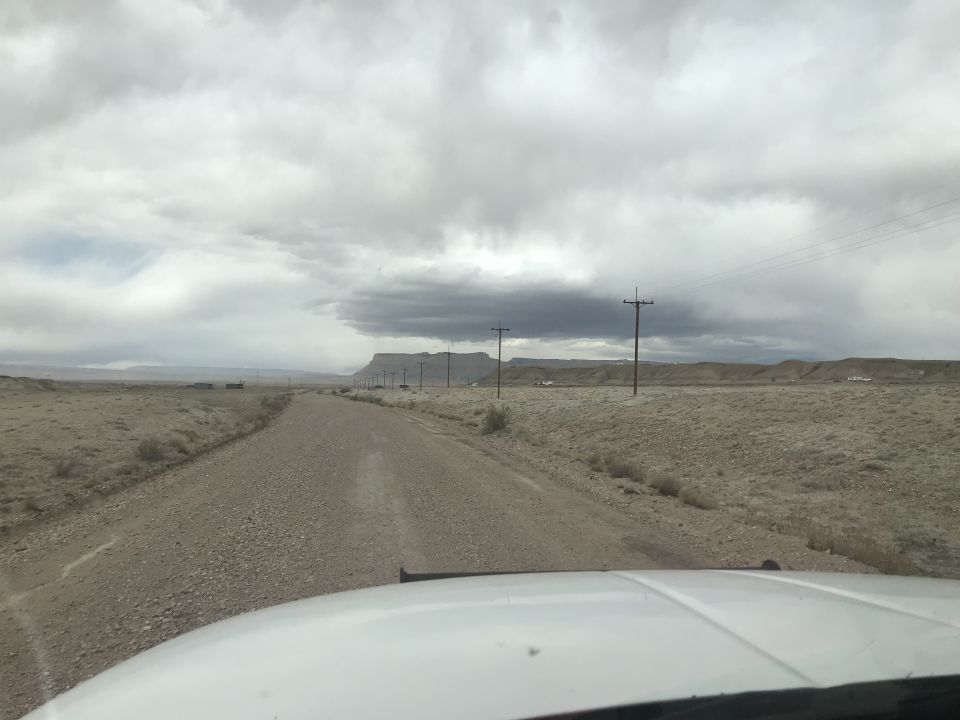 Dirt road in a desolate landscape with telephone poles and a cloudy sky.