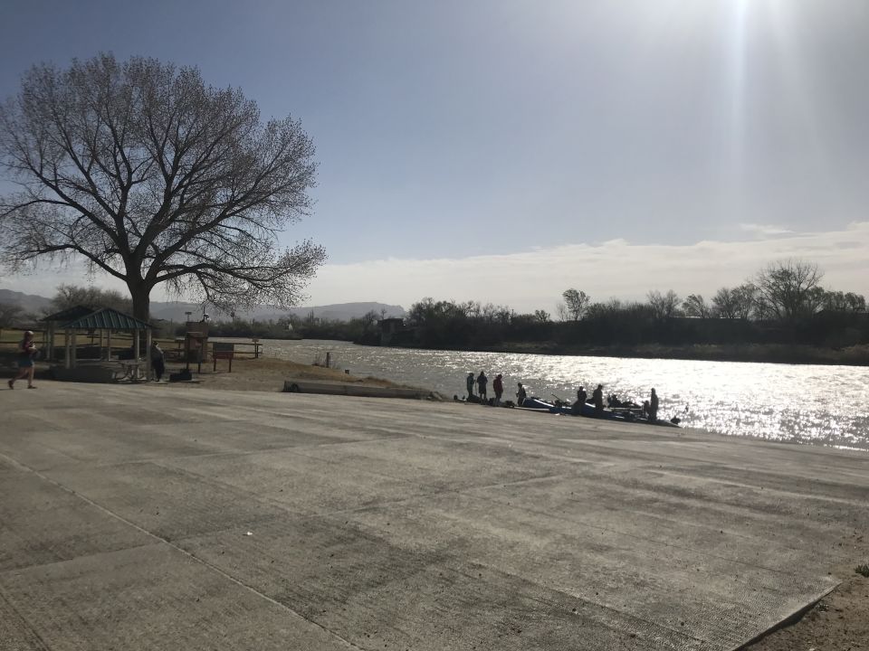 Concrete boat ramp leading to a river with people and kayaks.