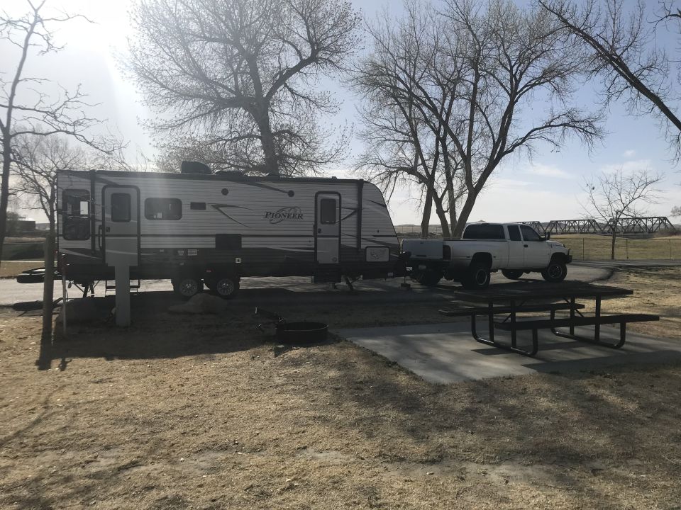 White pickup truck parked behind a travel trailer at a campsite with a picnic table in the foreground.