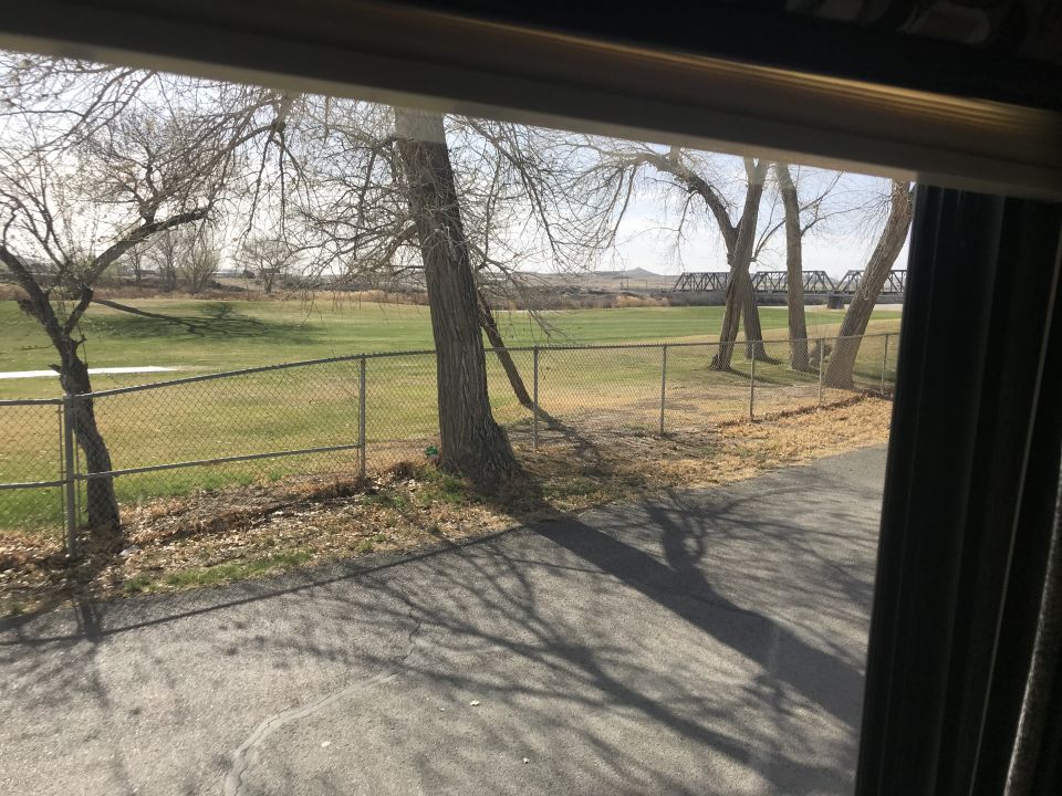 View of a field with trees and a railroad bridge through a window.